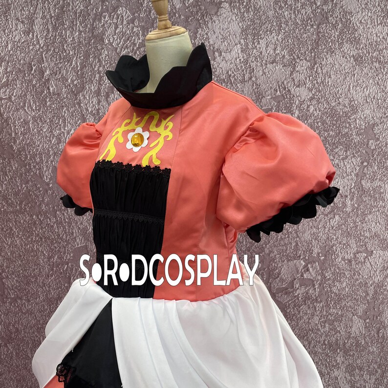 May include: A coral-colored cosplay costume with a black and white skirt. The top features a black collar and sleeves with a ruffled edge. The bodice has a black panel with yellow and white floral embroidery. The text "SOR DCOSPLAY" is visible.