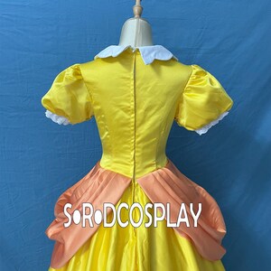 May include: A yellow satin dress with a white collar and peach-colored accents. The dress features short, puffed sleeves with white lace trim. The text "SORODCOSPLAY" is visible on the dress.
