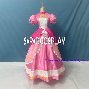 May include: A pink princess-style dress with short, puffy sleeves and a high collar. The bodice features gold embroidery and a jewel accent. The skirt is full, with white lace trim and gold accents. The text "SORODCOSPLAY" is visible.