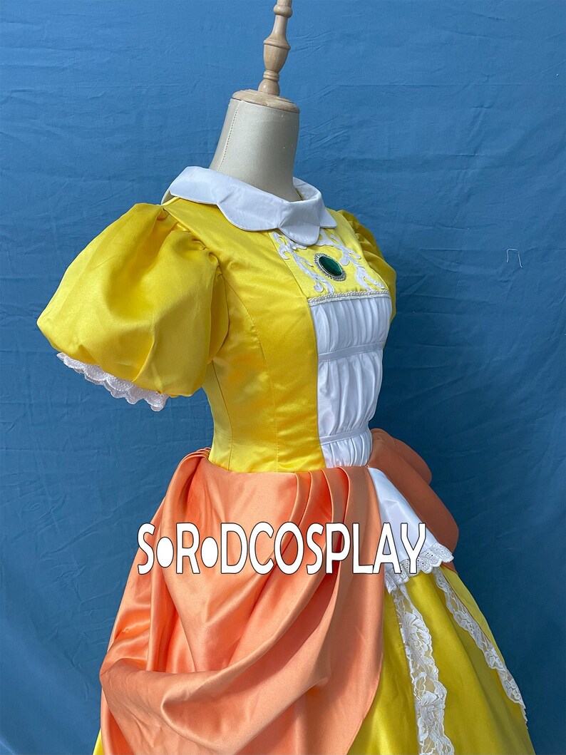 May include: A yellow cosplay dress with a white collar and puff sleeves. The bodice has white panels with decorative trim and a green jewel. An orange sash and skirt overlay add detail. The text "SORODCOSPLAY" is visible.