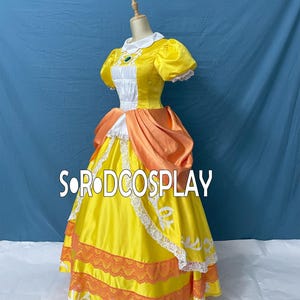 May include: A yellow and orange cosplay dress with white lace trim and a white collar. The dress features puff sleeves and a bodice with a green jewel. The text "SORODCOSPLAY" is visible on the dress.