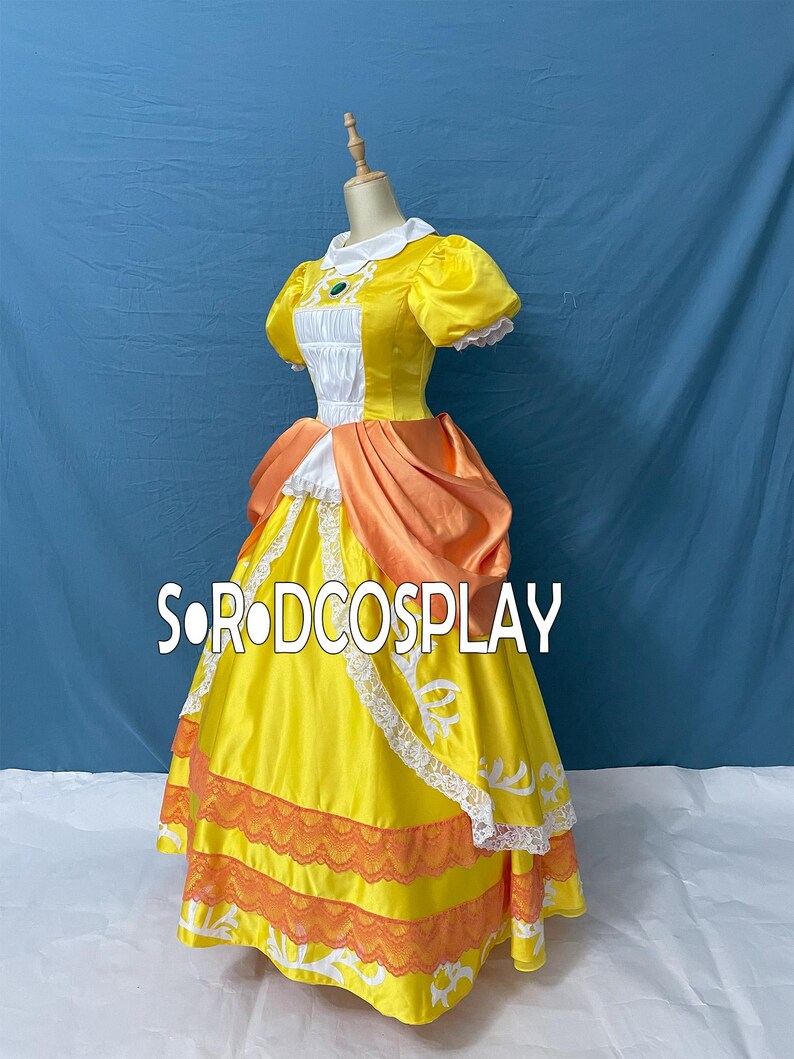 May include: A yellow and orange cosplay dress with white lace trim and a white collar. The dress features puff sleeves and a bodice with a green jewel. The text "SORODCOSPLAY" is visible on the dress.