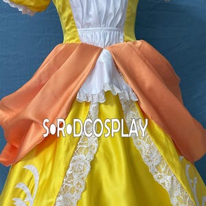 May include: A yellow cosplay dress with white lace trim and orange accents. The dress features a white bodice and a layered skirt. The text "SORODCOSPLAY" is visible on the front of the dress.