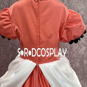 May include: A cosplay costume featuring a coral-colored bodice with short, puffed sleeves trimmed in black. The costume includes a white skirt and the text "S&bull;R&bull;DCOSPLAY". The back of the costume is visible, showing a zipper closure.