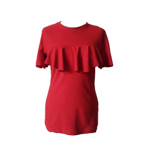 May include: A solid red t-shirt with a round neckline and short sleeves. The shirt features a horizontal ruffle detail across the chest. The garment is made of a soft, lightweight material.