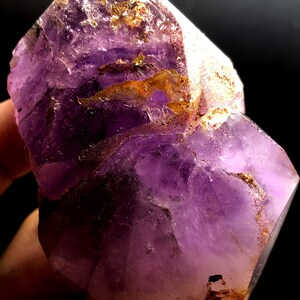 Pode incluir: Um grande cristal de ametista roxo com uma superfície áspera e natural. O cristal tem uma cor roxa profunda e é translúcido. Tem uma forma irregular única com vários pontos e facetas.
