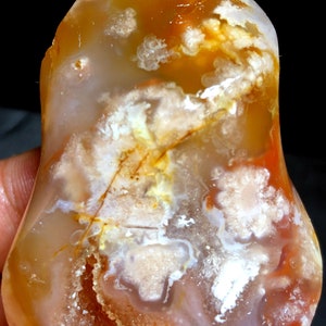 May include: A large, orange, white and red agate crystal with a pointed top and a smooth, rounded base. The crystal has a variety of patterns and textures, including swirls, bands, and inclusions.
