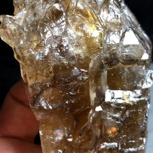 Pode incluir: Um grande cristal de quartzo transparente com uma tonalidade marrom fumada. O cristal tem muitas facetas e pontas, e é muito brilhante. O cristal tem cerca de 15 cm de altura.