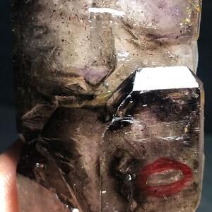 May include: A large, dark amethyst crystal with a smoky quartz point. The crystal has a purple hue with a smoky grey colour. The crystal is faceted and has a natural, rough texture.