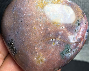 May include: A heart-shaped polished stone with a pink, brown, and white color pattern. The stone has a smooth, polished surface and a natural, organic shape.