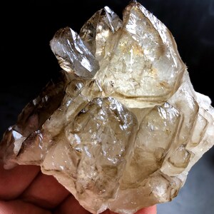 Pode incluir: Um aglomerado de cristais de quartzo fumado com uma variedade de formas e tamanhos. Os cristais são translúcidos e têm uma cor castanho claro.