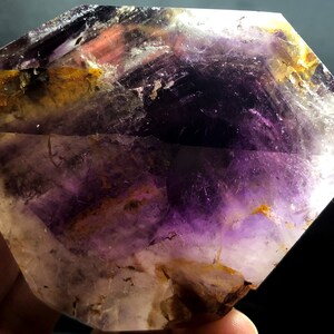 Pode incluir: Um grande cristal de ametista facetado com um padrão de cor roxo e amarelo. O cristal é transparente e tem uma superfície lisa e polida.