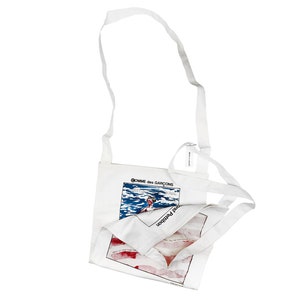 Peut inclure: Sac fourre-tout en toile blanche avec un imprimé graphique d'une personne nageant dans l'océan. Le texte "COMME des GARCONS" et "JUNYA WATANABE" est imprimé sur le sac.