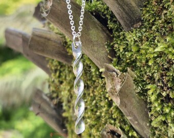 May include: A silver-colored pendant necklace with a twisted spiral design. The pendant hangs from a delicate chain. The background features a tree trunk covered in green moss.