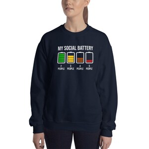 May include: Navy blue sweatshirt with white text that reads "My Social Battery" and shows a row of five battery icons with different levels of charge. The text below the icons reads "2 People, 3 People, 4 People, 5 People".