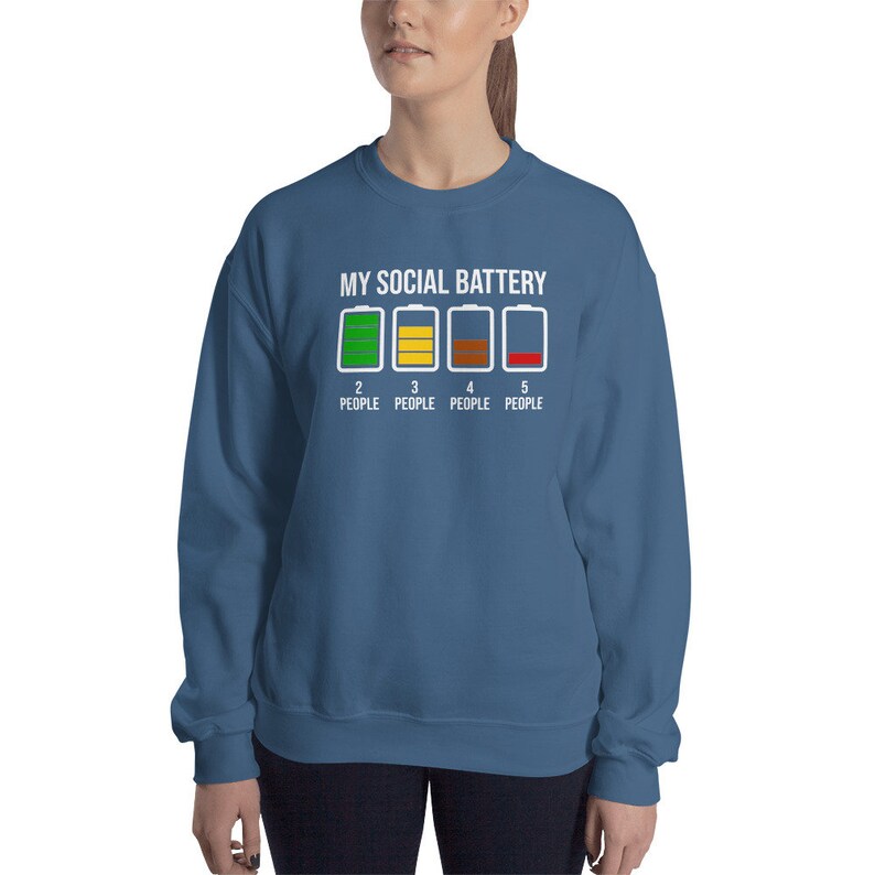 May include: A blue sweatshirt with the text "MY SOCIAL BATTERY" and a graphic of a battery with four levels of charge, each level representing a different number of people. The battery levels are green, yellow, brown, and red.