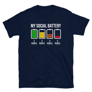 May include: A navy blue t-shirt with the text "My Social Battery" and a graphic of four battery icons. The battery icons are green, yellow, brown, and red, representing different levels of charge. The text "2 People", "3 People", "4 People", and "5 People" is below the battery icons.