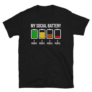May include: Black t-shirt with the text "My Social Battery" and a graphic of a battery meter with four levels. The battery meter is green, yellow, brown, and red. The text below the battery meter reads "2 People, 3 People, 4 People, 5 People".