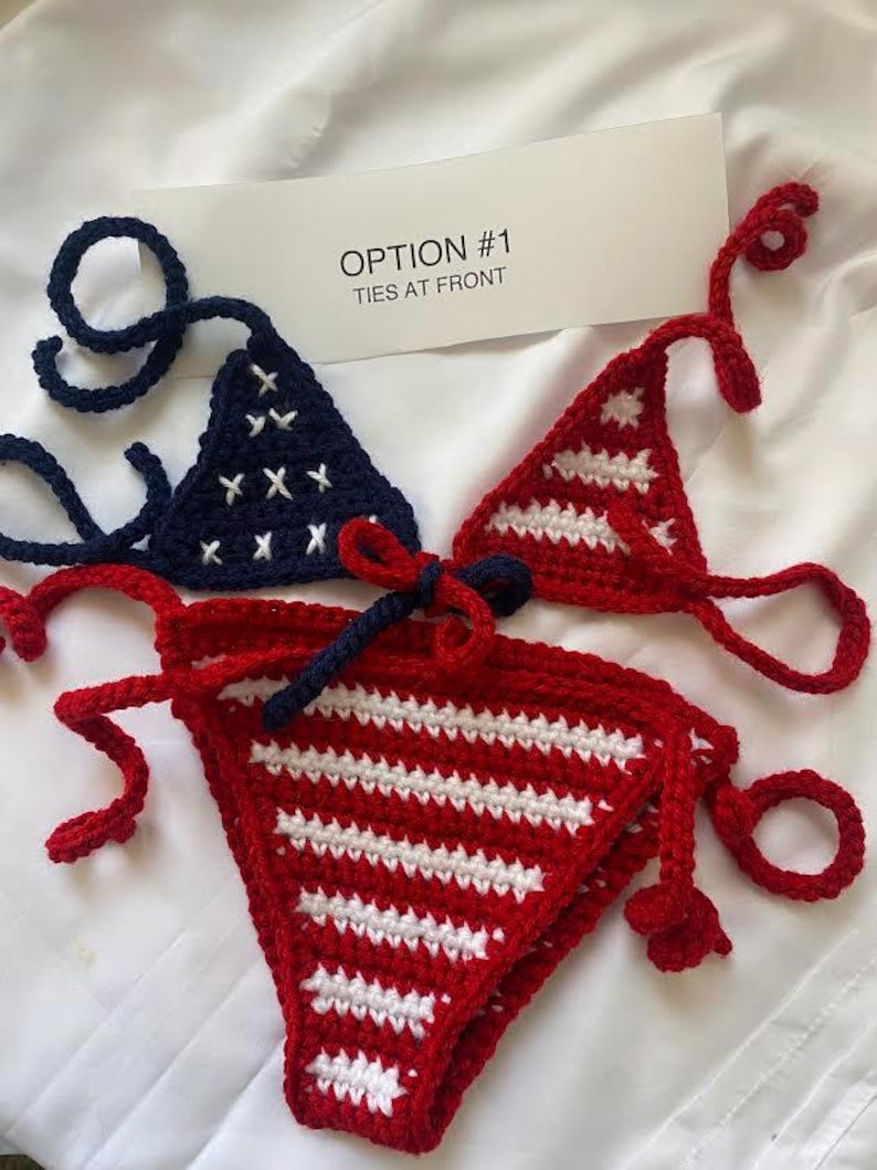 Puede incluir: Un conjunto de bikini de ganchillo que incluye un top triangular azul marino con estrellas blancas bordadas y un top triangular rojo con rayas horizontales blancas. La parte inferior es roja con rayas blancas y un lazo azul marino al frente. Texto: OPTION #1 TIES AT FRONT.