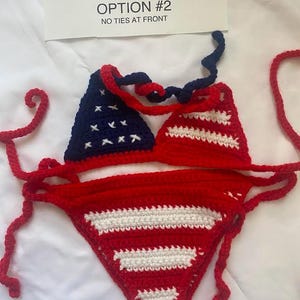 Puede incluir: Un conjunto de bikini de ganchillo de dos piezas con un patr&oacute;n de bandera estadounidense en rojo, blanco y azul. La parte superior tiene un tri&aacute;ngulo azul oscuro con estrellas blancas bordadas y otro a rayas rojas y blancas. La parte inferior es roja con rayas blancas. Texto: OPTION #2 NO TIES AT FRONT.