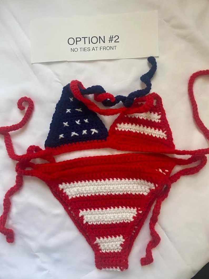 Puede incluir: Un conjunto de bikini de ganchillo de dos piezas con un patr&oacute;n de bandera estadounidense en rojo, blanco y azul. La parte superior tiene un tri&aacute;ngulo azul oscuro con estrellas blancas bordadas y otro a rayas rojas y blancas. La parte inferior es roja con rayas blancas. Texto: OPTION #2 NO TIES AT FRONT.