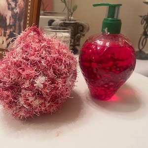 May include: A pink and white fluffy bath pouf next to a red liquid soap bottle with a green pump dispenser.