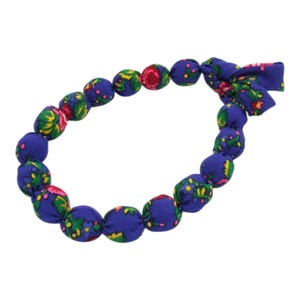Puede incluir: Un collar de tela azul con un estampado floral en verde, rosa y amarillo. El collar está hecho de cuentas redondas cubiertas de tela y se ata con un lazo de tela a juego. Las cuentas tienen aproximadamente 2,5 cm de diámetro.