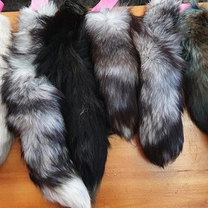 Può includere: Una collezione di code di volpe in vari colori, tra cui bianco, nero, grigio e marrone. Le code sono esposte su una superficie di legno, con etichette rosa attaccate alla parte superiore di ogni coda.