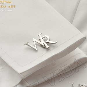 May include: A pair of silver cufflinks with the initials "WR" engraved on them. The cufflinks are shown on a white shirt cuff.