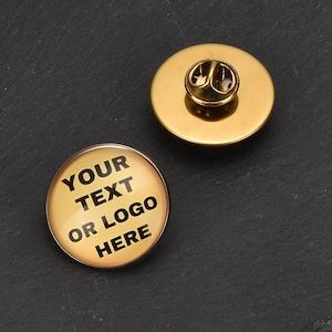 May include: A gold-colored pinback button with a clear plastic cover. The button has the text "YOUR TEXT OR LOGO HERE" printed in black on a gold background.