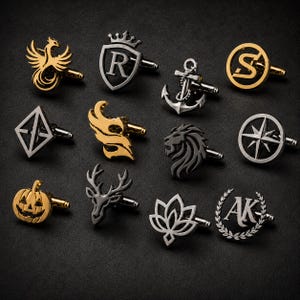 May include: A collection of twelve metal cufflinks featuring various designs including a phoenix, a shield with the letter R, an anchor, the letter S, a diamond shape, flames, a lion head, a compass, a pumpkin, a deer head, a lotus, and the letters AK.