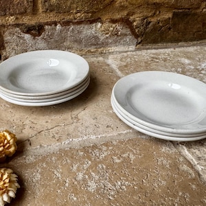 May include: Two stacks of white ceramic plates, each stack containing three plates. The plates are plain and have a slightly textured surface.
