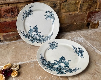May include: Two antique white plates featuring detailed teal floral and scrollwork patterns. The plates have a slightly aged look, enhancing their vintage appeal. Ideal for collectors or to add a touch of elegance to a dining table.