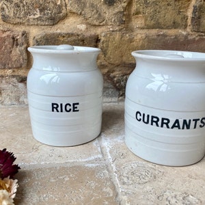 May include: Two white ceramic storage jars with black lettering. The jar on the left says "RICE" and the jar on the right says "CURRANTS".