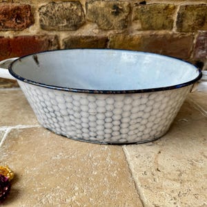 May include: Oval, white enamel basin with a honeycomb pattern and black trim. The basin has two white handles and a light blue interior. A vintage kitchenware item.