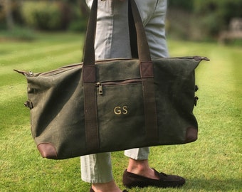 Pode incluir: Uma bolsa de viagem de lona verde com detalhes em couro marrom e um bolso com zíper. A bolsa tem um monograma personalizado "GS" na frente.