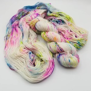 Op de afbeelding: Een bol wit garen met kleurrijke spikkels in roze, blauw, groen en geel.