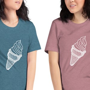Puede incluir: Dos mujeres vistiendo camisetas con un contorno blanco de un cono de helado en la parte delantera. La mujer de la izquierda lleva una camiseta azul verdosa y la mujer de la derecha lleva una camiseta rosa.