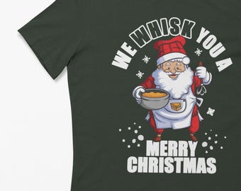Könnte beinhalten: Dunkelgrünes T-Shirt mit einem Cartoon-Weihnachtsmann, der eine Schüssel und einen Schneebesen hält. Der Text "We Whisk You a Merry Christmas" ist in Weiß gedruckt. Das Design umfasst Schneeflocken und eine Kochschürze.