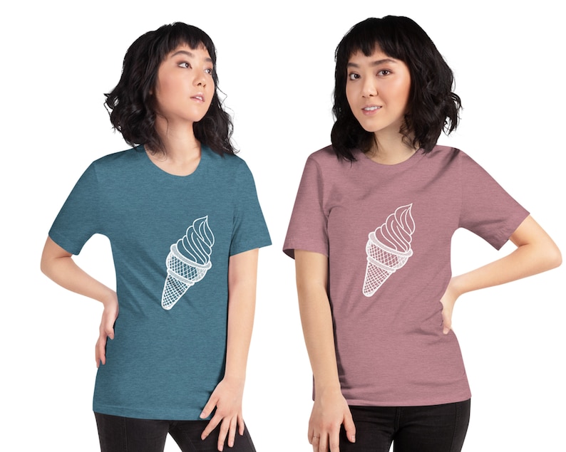Puede incluir: Dos mujeres vistiendo camisetas con un contorno blanco de un cono de helado en la parte delantera. La mujer de la izquierda lleva una camiseta azul verdosa y la mujer de la derecha lleva una camiseta rosa.
