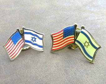 May include: Two metal pins featuring the flags of the United States and Israel. The American flag pin has red and white stripes with a blue field of stars. The Israeli flag pin is white with a blue Star of David.