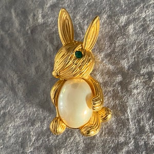 May include: A gold-tone rabbit brooch with a white pearl center and green rhinestone eyes.