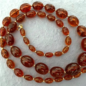 May include: A long amber necklace featuring oval-shaped beads and gold accents. The necklace is crafted from natural amber and is a stunning piece of jewellery.
