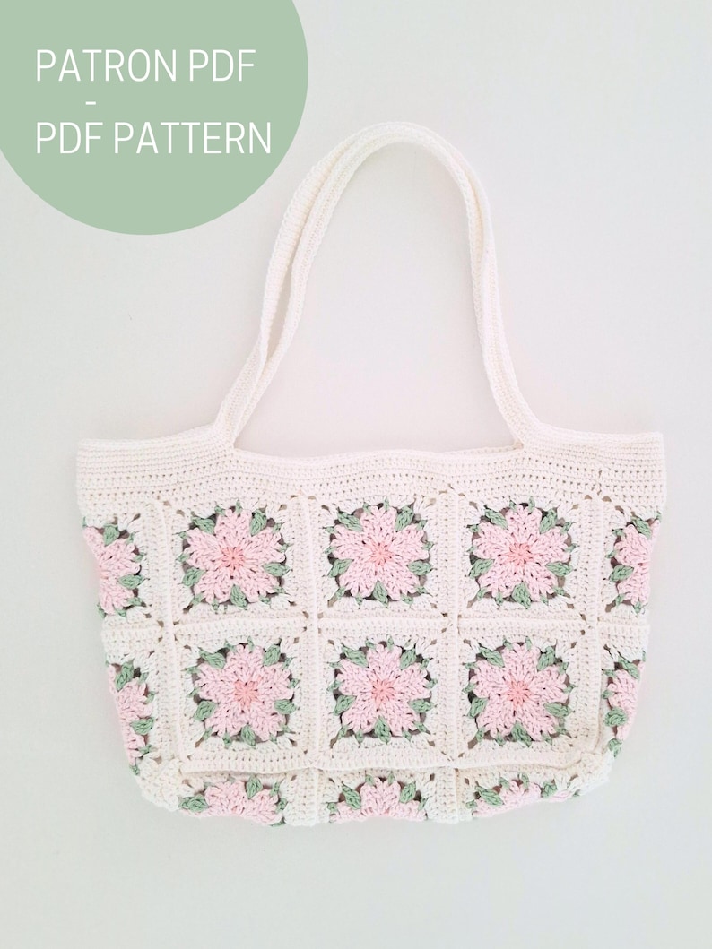 K&ouml;nnte beinhalten: Wei&szlig;e H&auml;kel-Tragetasche mit rosa und gr&uuml;nen Blumenquadraten. Die Tasche hat zwei Henkel und ist mit einem Granny-Square-Muster gearbeitet.