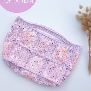May include: A crocheted tote bag with a light purple and pink color gradient. The bag is made of square granny squares with a flower design in the center of each square. The bag has a wide opening at the top and a flat bottom.