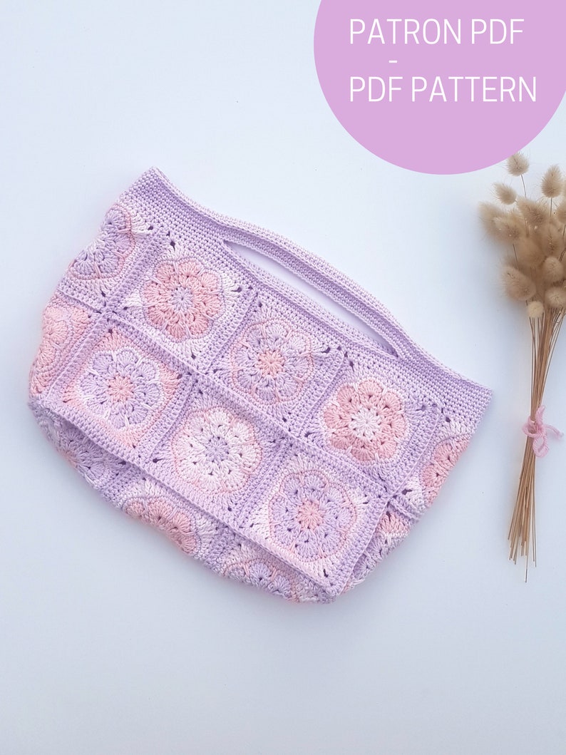 May include: A crochet bag with a pink and purple color scheme. The bag is made of granny squares with a flower design. The bag has a wide opening and a handle.