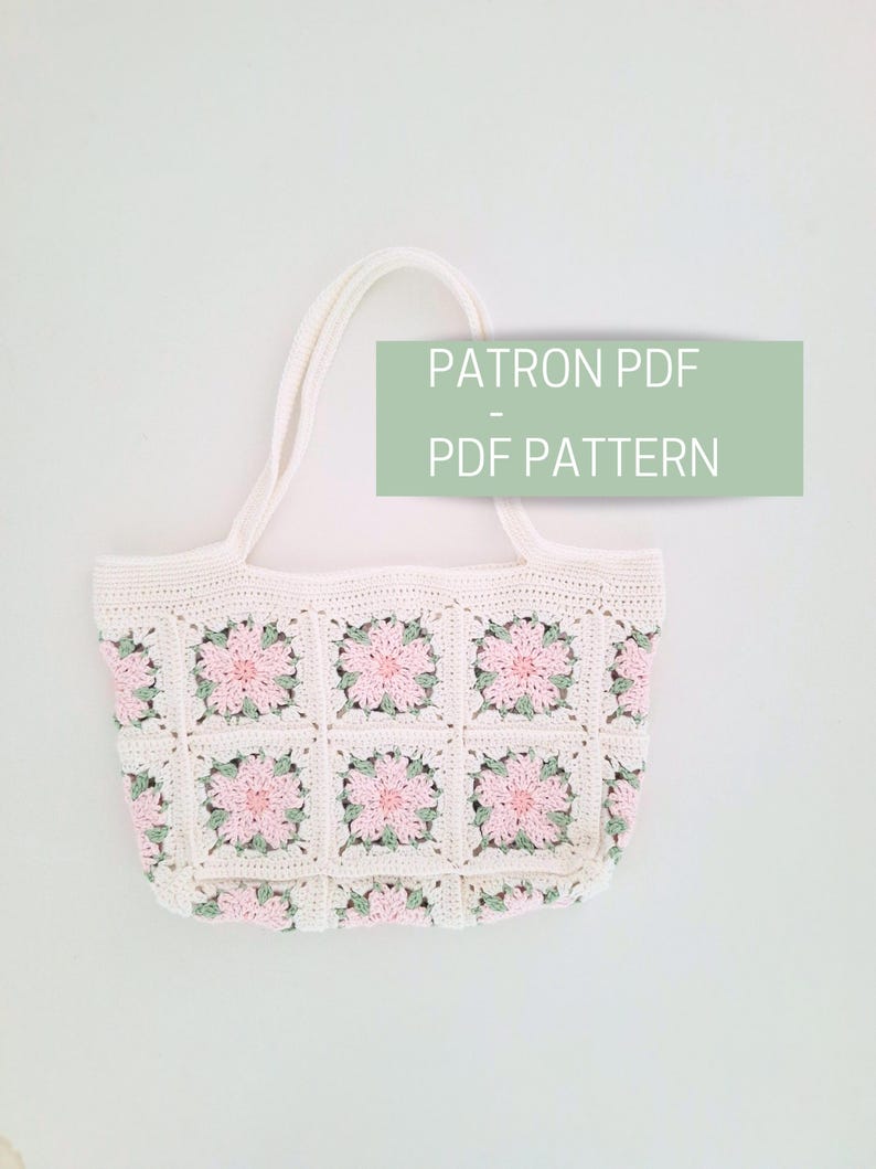 K&ouml;nnte beinhalten: Wei&szlig;e H&auml;kel-Tragetasche mit rosa und gr&uuml;nen Blumenquadraten. Die Tasche hat zwei Henkel und tr&auml;gt den Schriftzug "PATRON PDF - PDF PATTERN" auf einem gr&uuml;nen Rechteck.