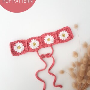 May include: A pink crocheted headband with white daisy flowers. The headband has two long ties.