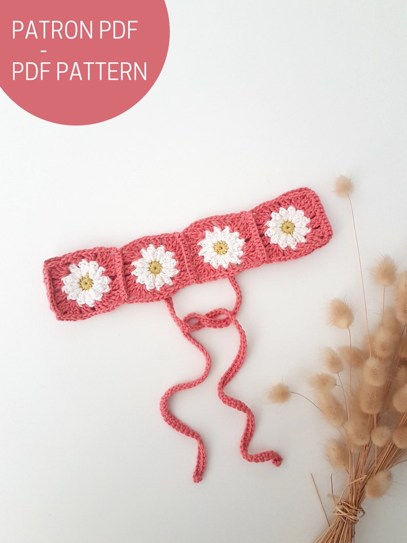 May include: A pink crocheted headband with white daisy flowers. The headband has two long ties.