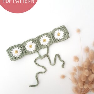 May include: A green crocheted headband with white daisy flowers. The headband has two long ties that can be tied at the back of the head.